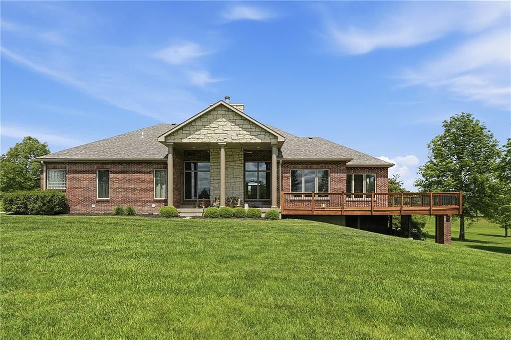 Rear elevation of 26619 K68 Hwy, showing the gable peak with stone-trimmed columns, a refinished cedar deck with new posts and lighting, and the long view across the back lawn
