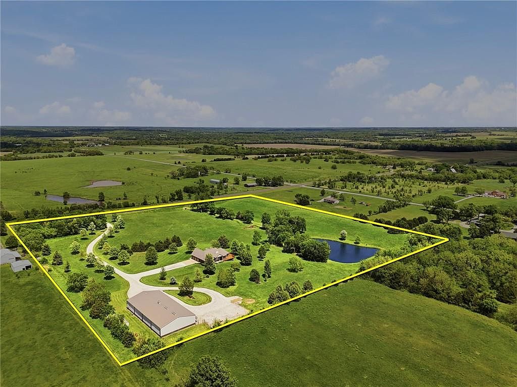 Aerial photograph of 26619 K68 Hwy with the 17.06 acre property boundary highlighted, showing the brick residence, the cream-colored commercial-grade outbuilding, the pond, and rolling Kansas farmland on every horizon