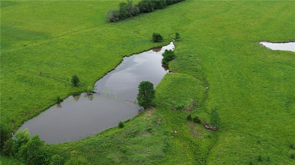 Aerial close-up of the stocked pond and surrounding pasture, showing the curving shoreline, a smaller upper pond, and the open green expanse of the back acreage