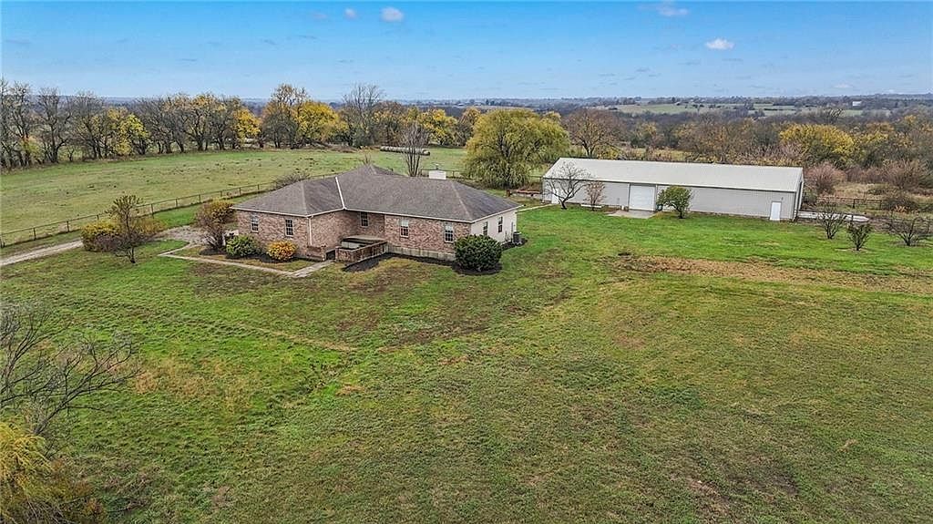 Wide aerial of the property in autumn light, showing the brick home, the white commercial-grade outbuilding behind it, and the open Kansas horizon stretching for miles